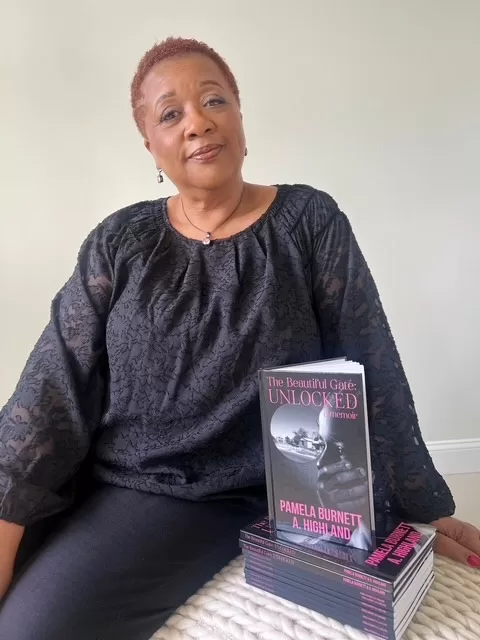 Pamela Burnett sitting with a stack of her newly published memoir The Beautiful Gate: Unlocked for purely decorative purposes only.